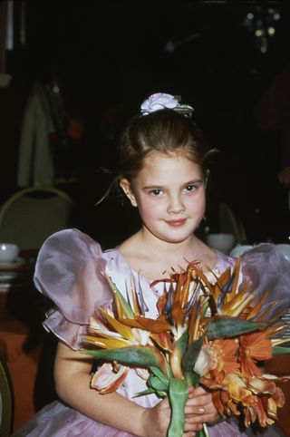 merican child actress Drew Barrymore holds a bouquet of flowers as she attends the 40th Annual Golden Globe Awards in support of her film 'E.T. the Extra-Terrestrial', Los Angeles, California, January 29, 1983.