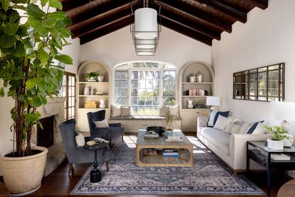 vaulted living room with dark wood ceiling and white walls with white sofa traditional rug and grey armchairs and big houseplant