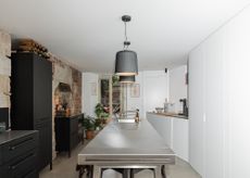 A stainless steel lighting in a kitchen with dark black cabinets opposite the island. Above the island are two shaded pendant lighting hanging 