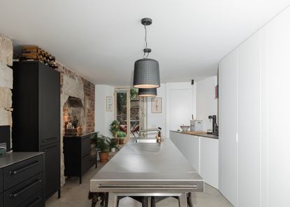 A stainless steel lighting in a kitchen with dark black cabinets opposite the island. Above the island are two shaded pendant lighting hanging
