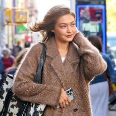 Gigi Hadid wearing a tan coat, baggy jeans, a cow-print bag, and Ugg boots