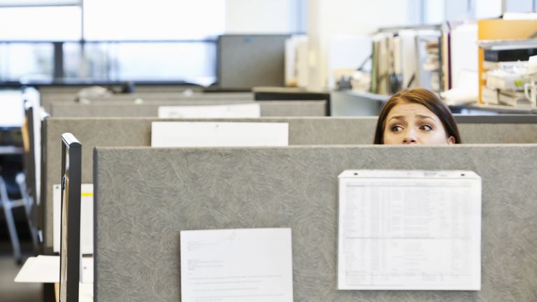 Woman peeping over desk partition in office