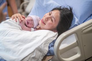 A woman smiles and cuddles her minutes-old newborn baby.