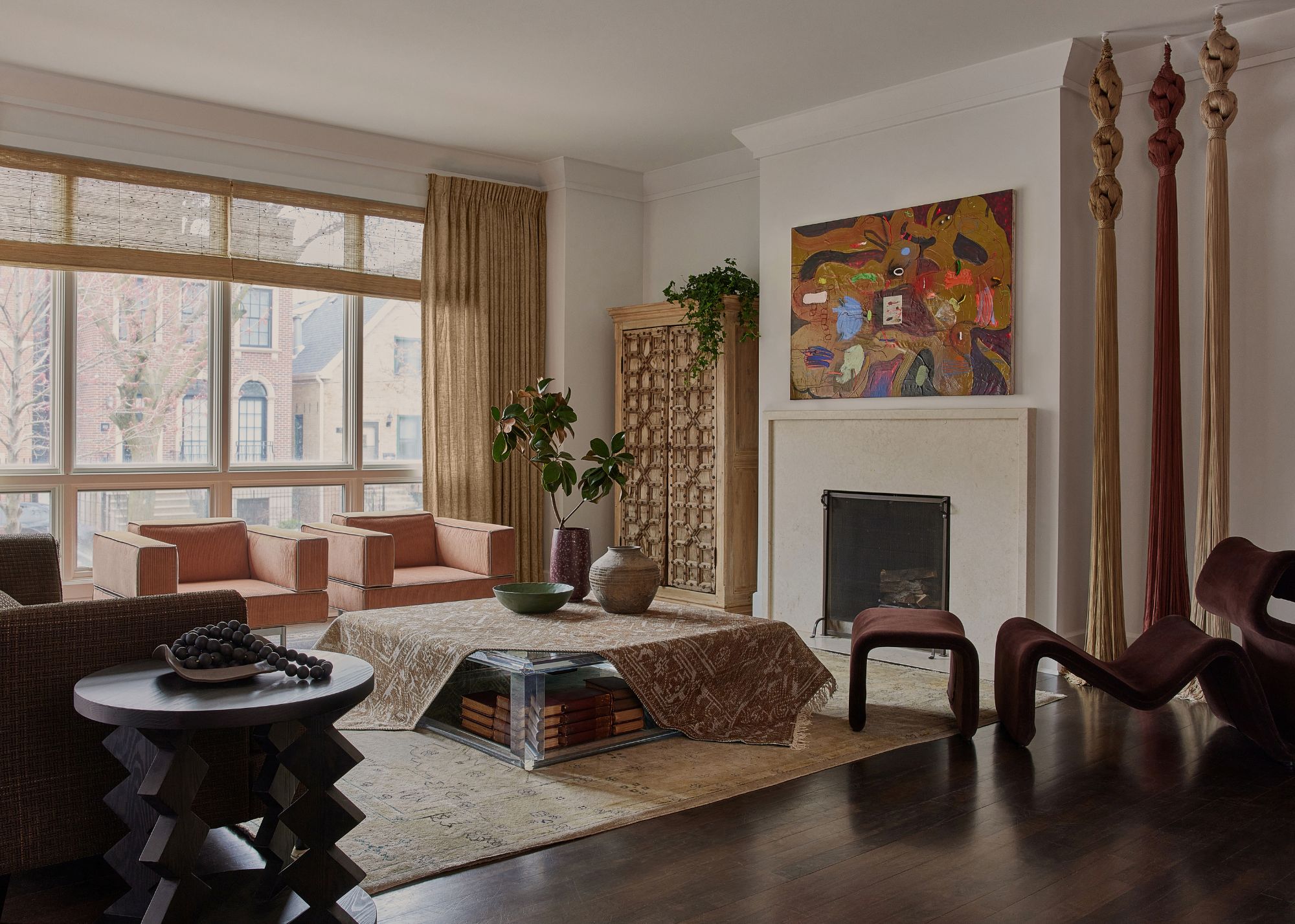 A living room with vintage carpet, a plum-toned accent chair, salmon-colored armchairs and a carpet strewn on the coffee table