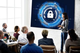 Business classroom with a woman talking about cyber security, blue padlock image on whiteboard