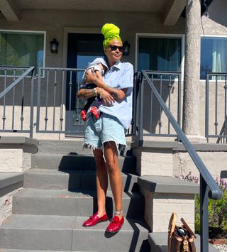 Crystal Anderson holding her baby in a button down, shorts, and red shoes