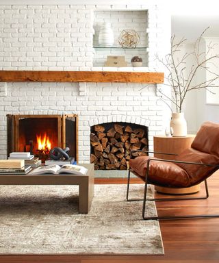 A living room with a white brick walll, a fireplace with logs next to it, a wooden coffee table, and a brown leather armchair