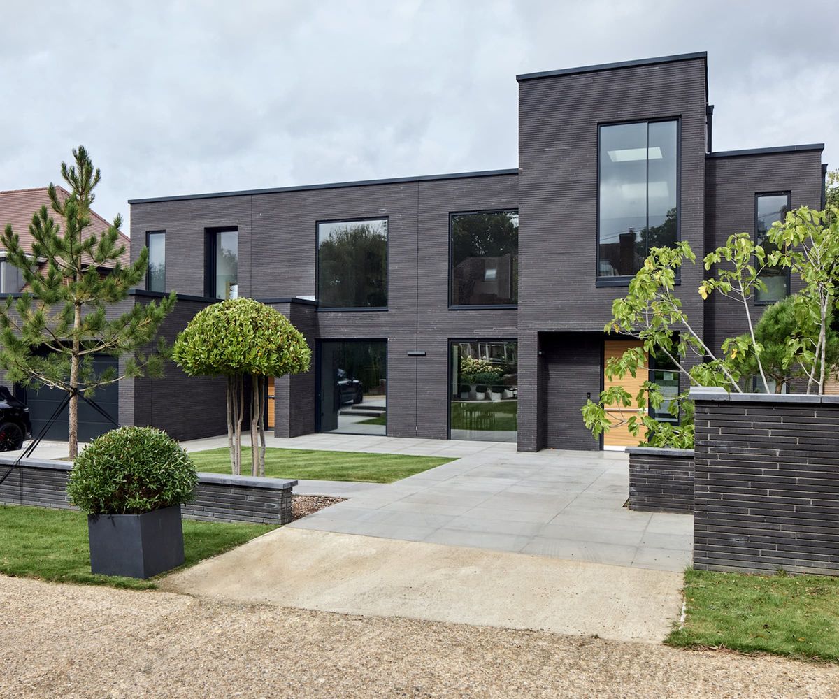 The front driveway of a house with a black facade with a wooden effect front door