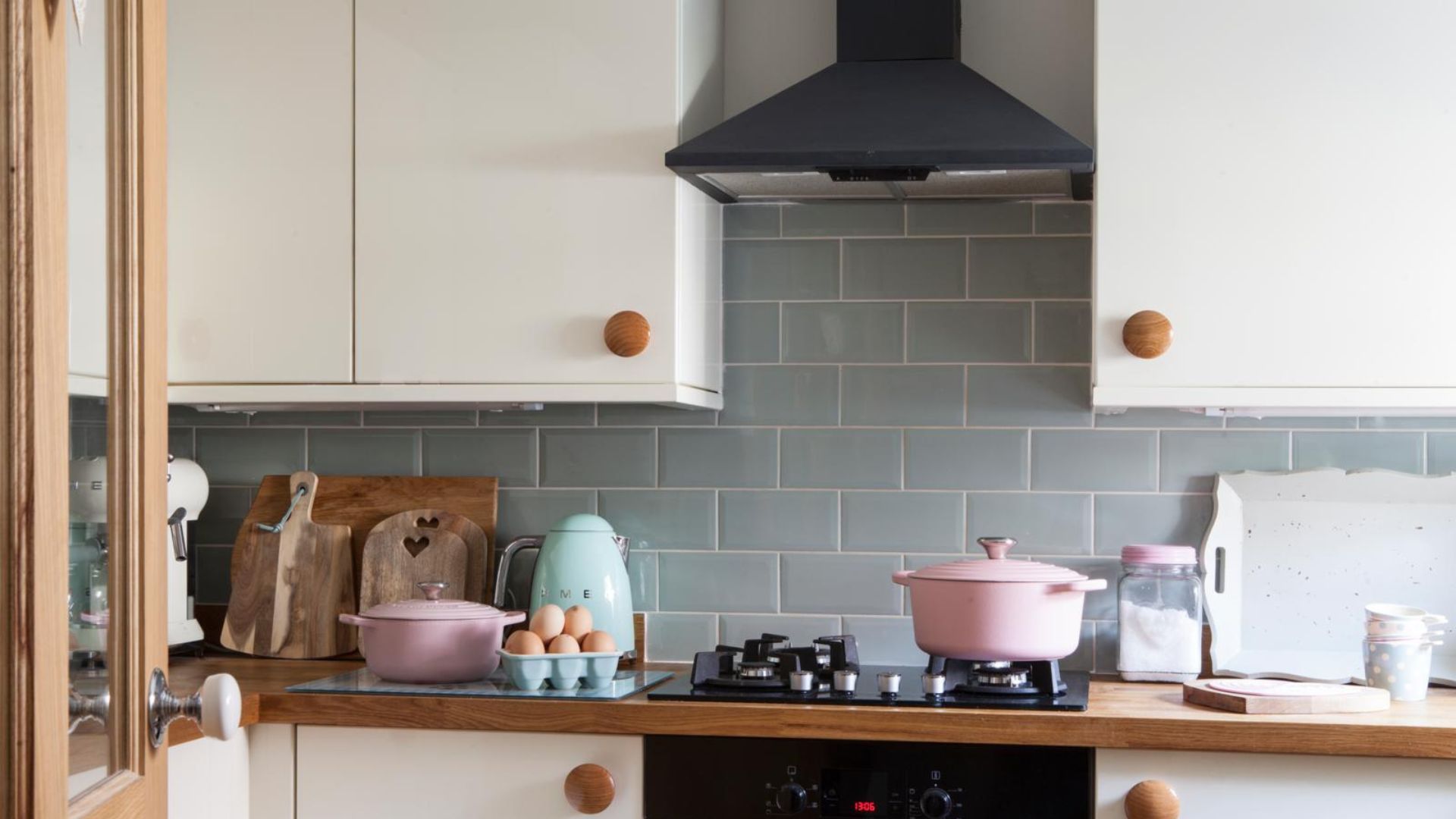 Oven with oven hood overhead, pastel appliances and cooking tools on the wooden counter