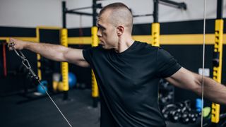 Man performs lateral raise using cable machine in gym