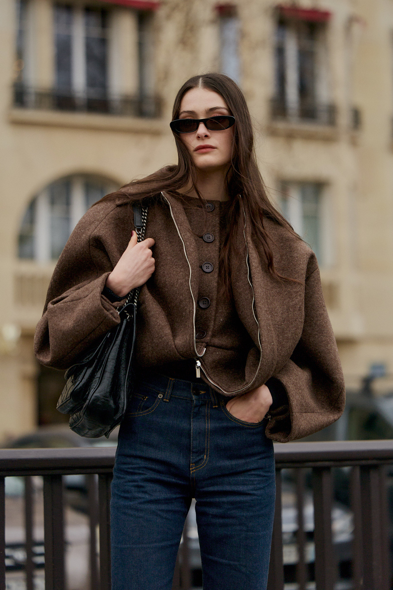 Woman in dark rinse jeans, brown crop jacket, and black hobo bag