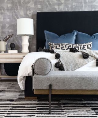 A bedroom with a black and white striped rug, black bedframe and blue pillows