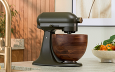 A dark green stand mixer on a countertop with a wooden bowl