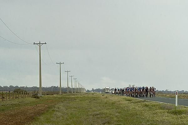 The peloton make their way along a straight section of wind-swept roads nearing the final twenty kilometres of stage three.