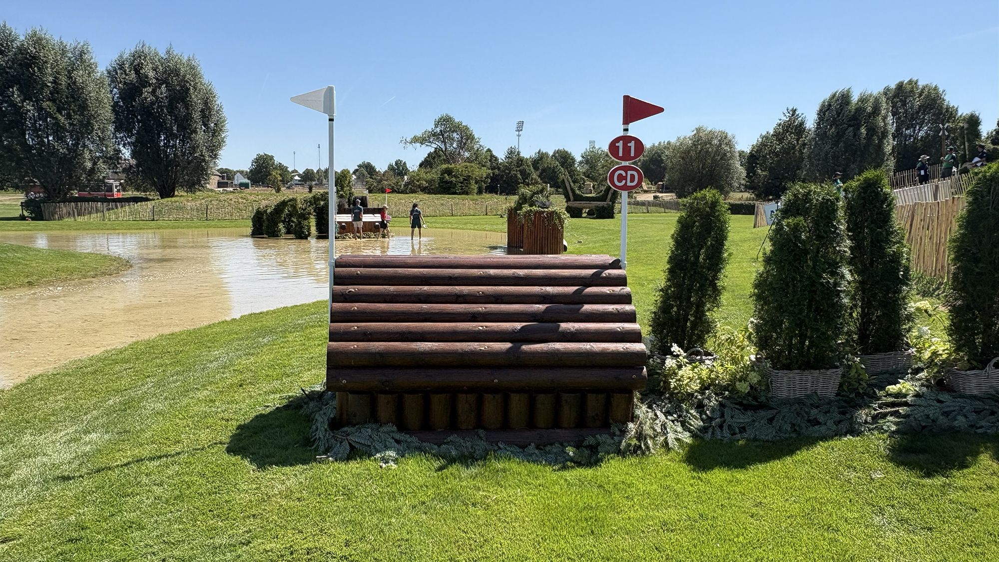 A wooden cabin fence in front of a water complex on the eventing World Championships cross-country course