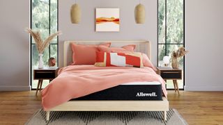 The Allswell Cool Mattress shown on a light wooden bed frame and dressed with peach colored linens and pillows