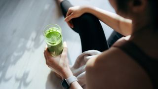 A woman in exercise clothing holding a glass of cucumber juice