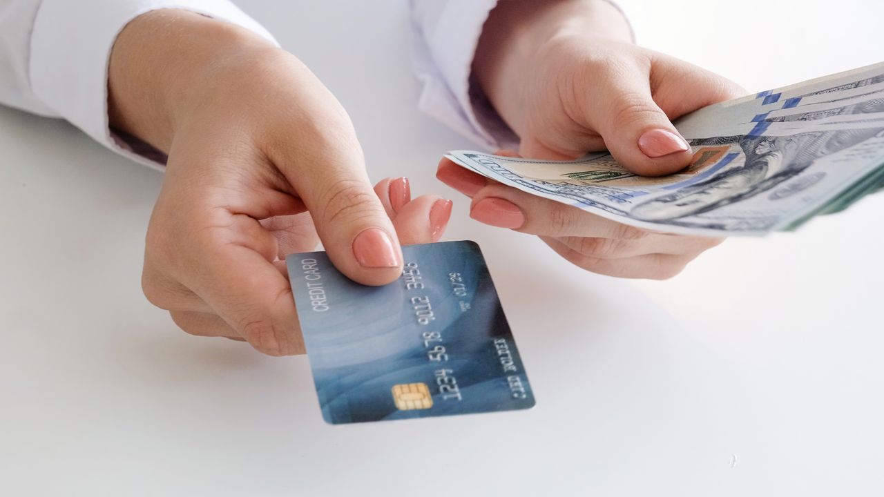 A woman&#039;s hand holds a cash back credit and U.S. hundred dollar bills.