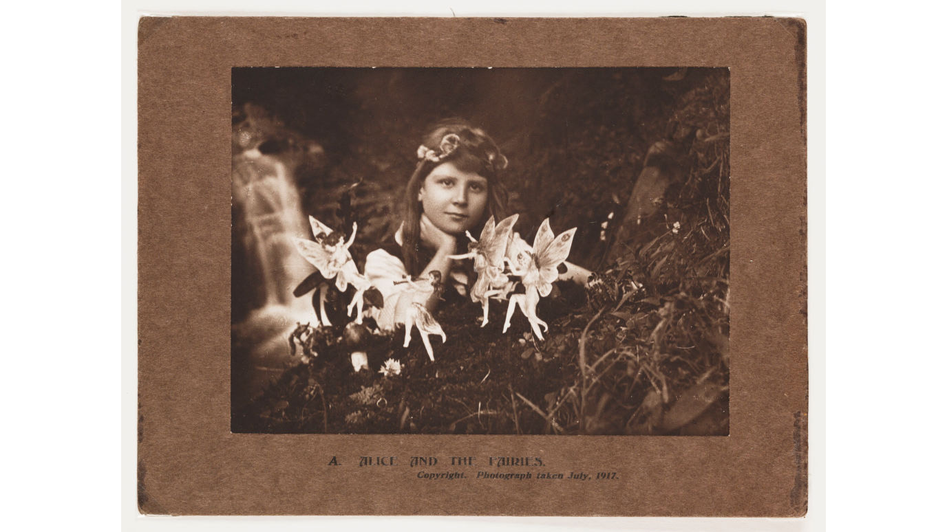 ENGLAND : A photograph of Frances 'Alice' Griffiths (1907-1986) taken by her cousin Elsie 'Iris' Wright (1901-1988), using her father Arthur's Midg quarter-plate camera, the first in the 'Cottingley Fairies' series. Frances, posed in the family garden, stares into the camera past dancing fairies, one of whom plays a pipe. A small waterfall tumbles into a 'beck', (dialect for ?stream?), beyond. The fairies were actually drawings by Elsie, secured in the ground with hat pins. It was a secret the girls decided to keep until the 1980s - once they realised the extent of the deception - to protect the public reputations of those who believed in the 'truth' of the images. Alice was probably the name given to Frances by Sir Arthur Conan Doyle (1859-1930) in an attempt to conceal the girls' identities when he published the photographs. (Photo by SSPL/Getty Images)