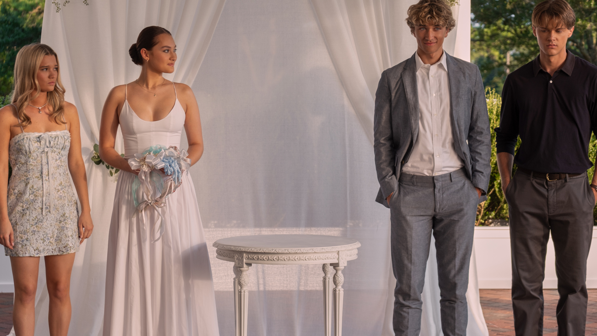 belly wears a white dress and stands by taylor while looking over and conrad and jeremiah in a still from the summer i turned pretty season 3
