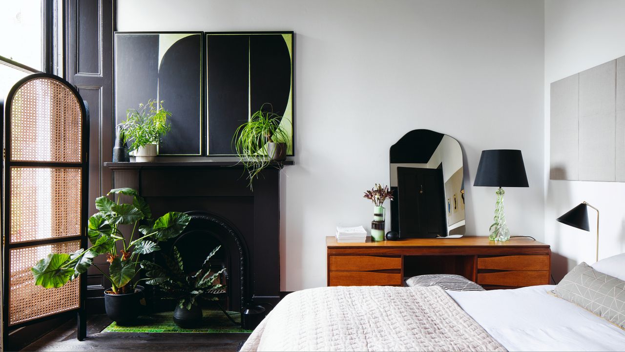 White painted bedroom with white bedding and grey accent throw and cushion, assortment of house plants on fireplace mantelpiece