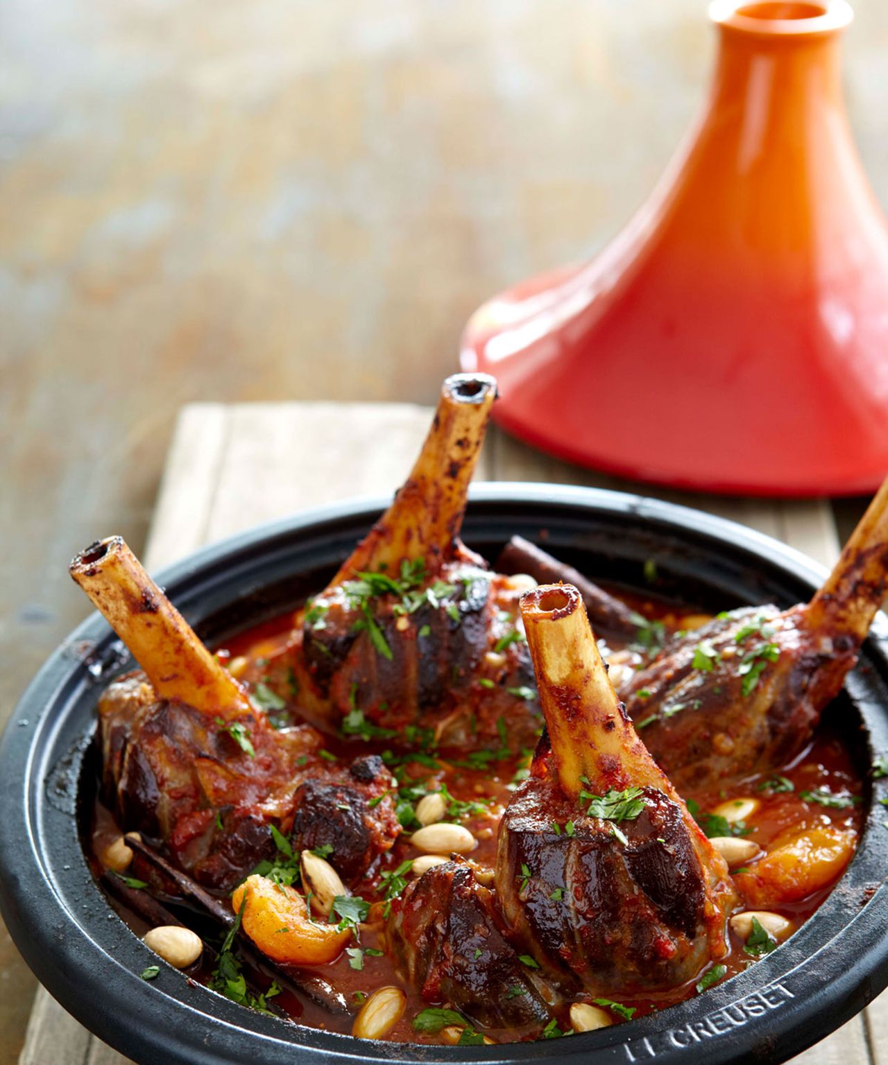Four lamb shanks cooked in red/orange and black earthenware Tagine