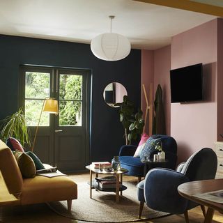 Living room with pink and navy walls, yellow and navy couches, a coffee table and plants