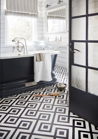 monochromatic bathroom with patterned floor tiles and Crittall style door and black freestanding bath