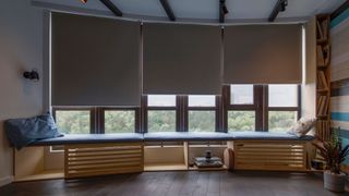 Three roller-style blackout blinds, half-closed with green trees visible outside the window
