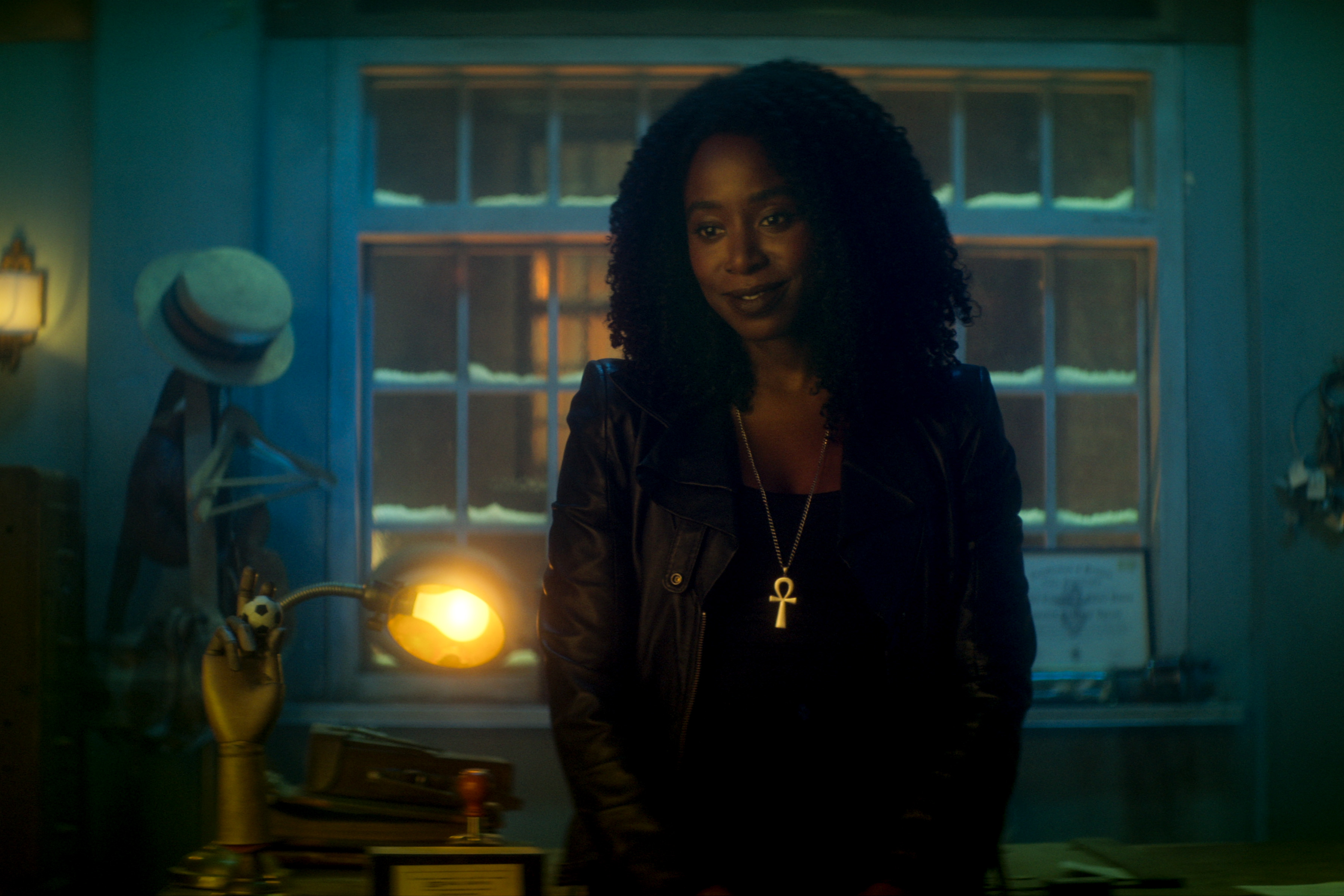 Kirby Howell-Baptiste as Death, standing in an office in front of a window, in episode 1 of DEAD BOY DETECTIVES
