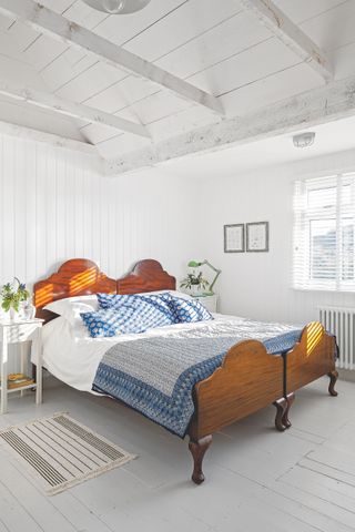 Bedroom with bed, white painted wood floor, area rug, white walls and white vaulted ceiling