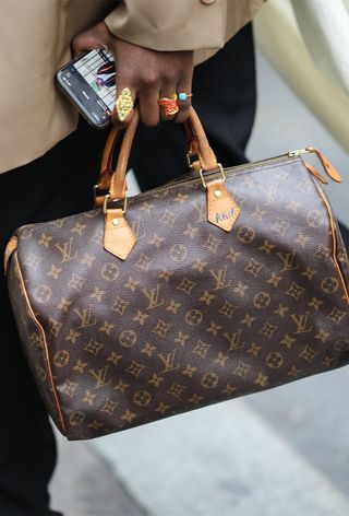 a close street-style photo of a woman wearing a vintage Louis Vuitton speedy bag with a tan blazer and black jeans