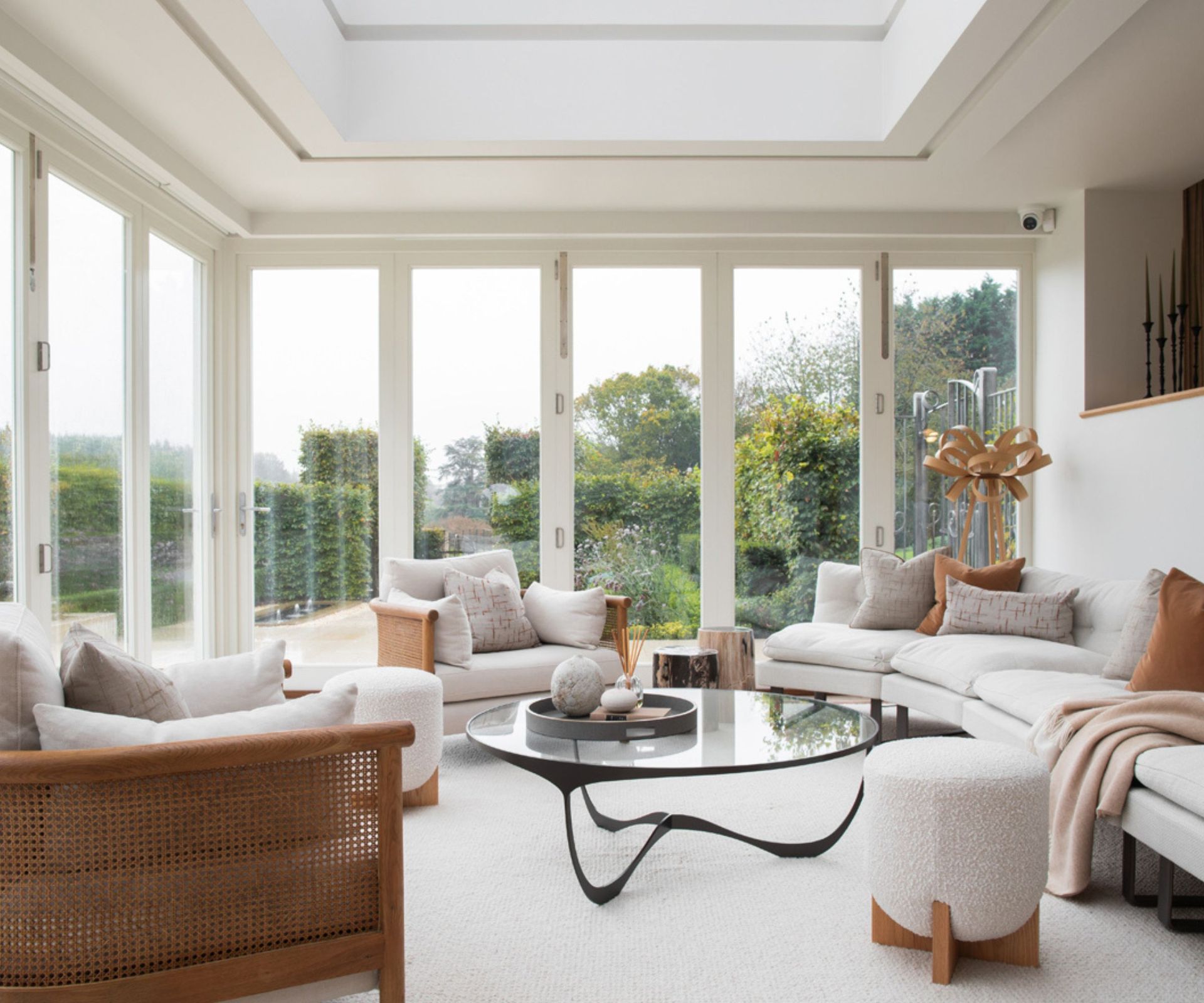 Living room decorated in neutral colors, with furniture in natural wood tones added. Floor to cieling windows offer a view to the garden, creating a relaxing atmosphere