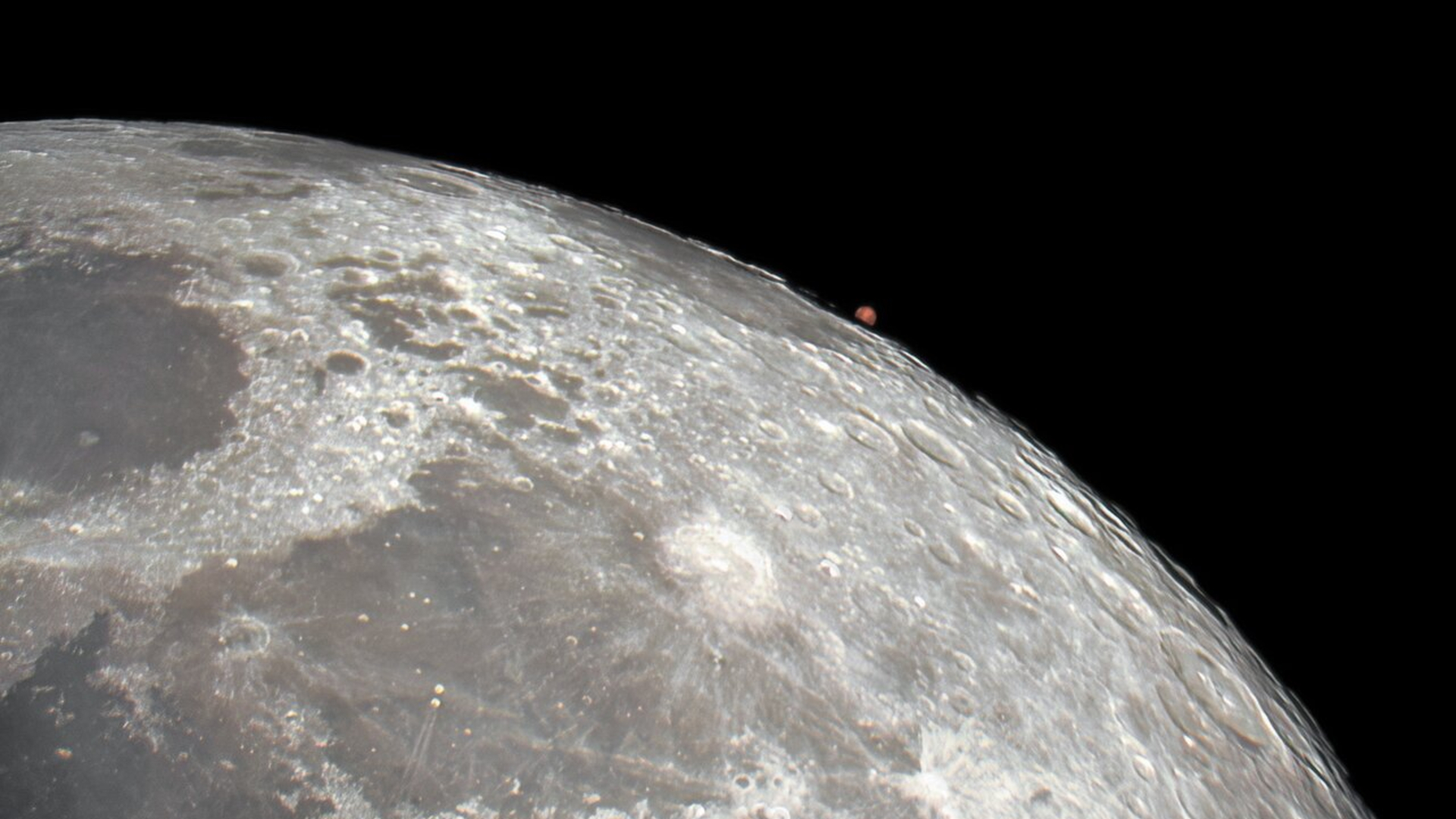 A close up of the surface of the moon with a small red dot hovering over its surface, which is the planet Mars