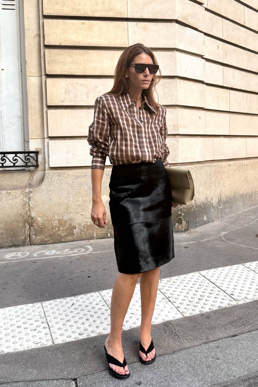 A woman wearing a brown plaid flannel tucked into a black pony hair pencil skirt, styled with thong wedges and a clutch bag.
