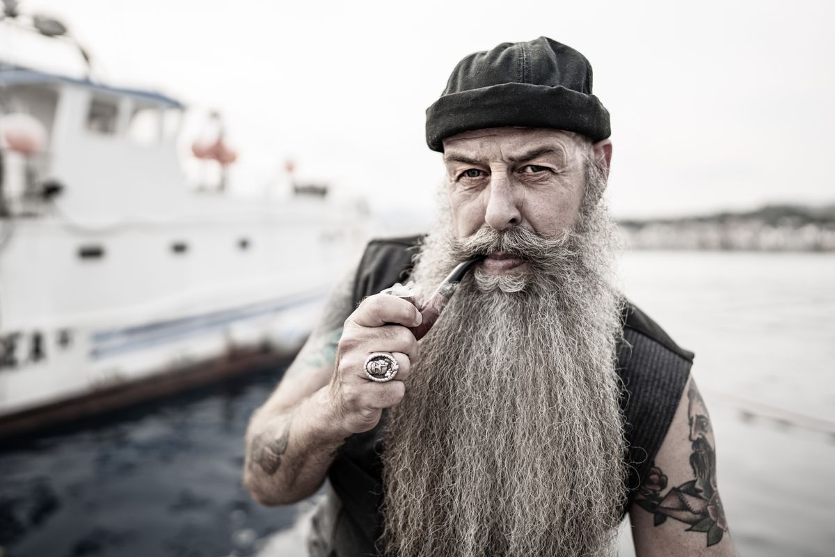 Bearded, tattooed man smoking a pipe aboard a boat