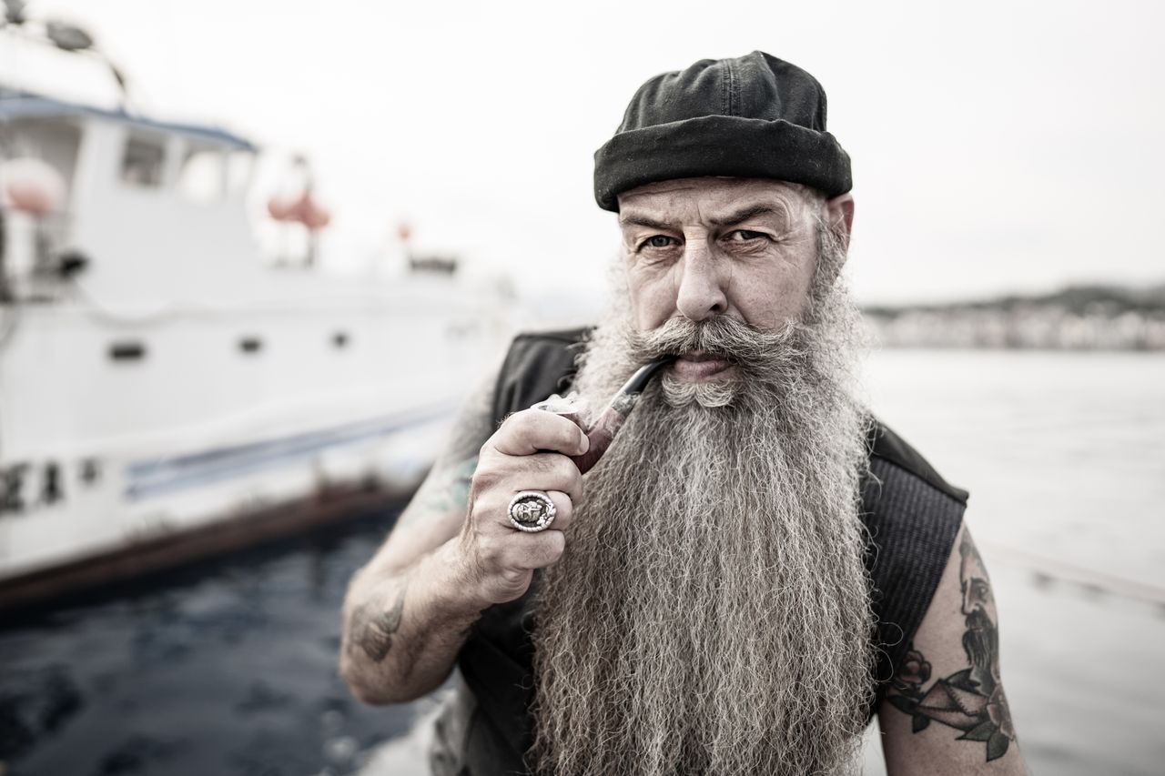 Bearded, tattooed man smoking a pipe aboard a boat