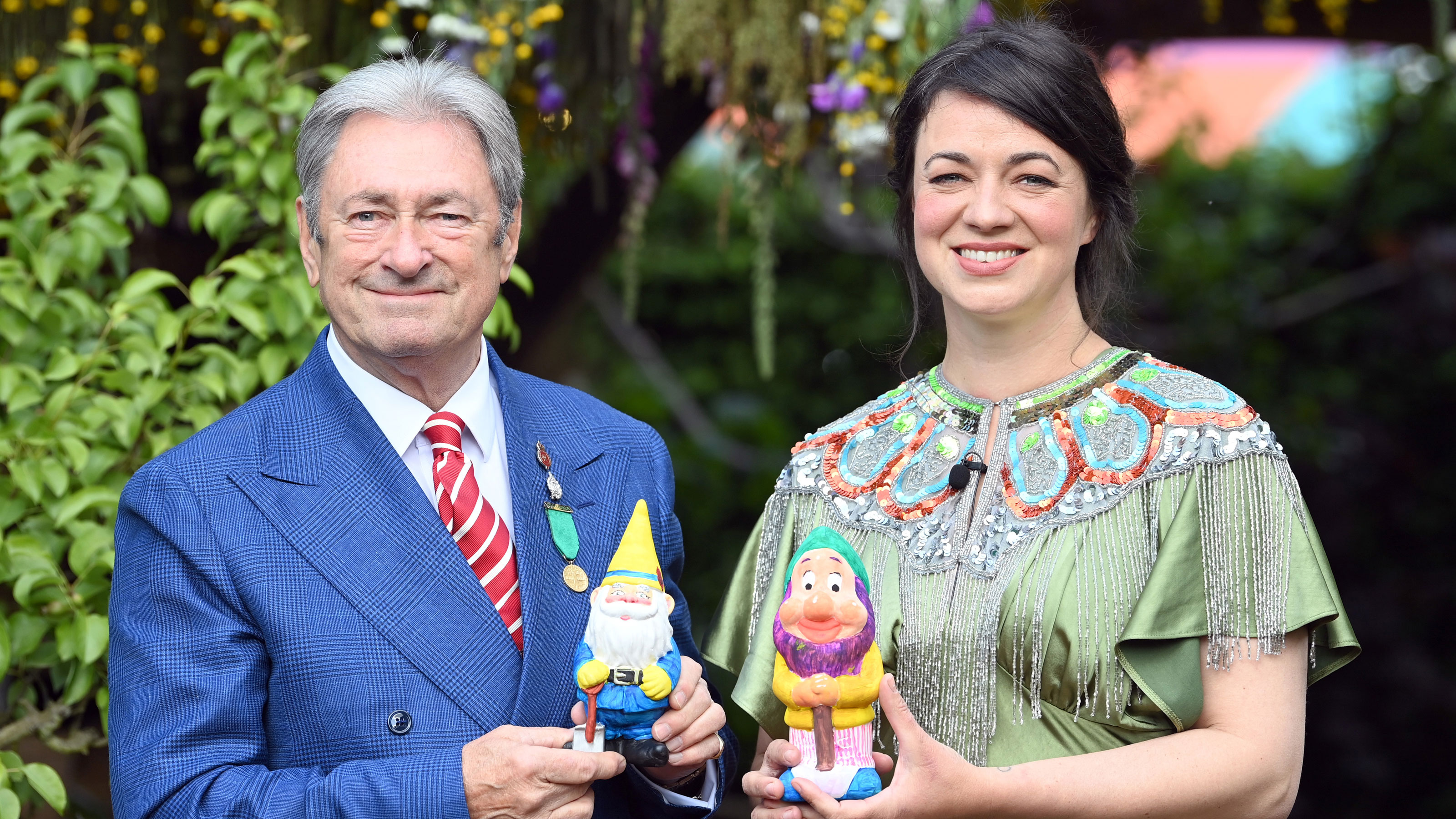 Frances Tophill in a green dress stood with Alan Titchmarsh in a blue suit, holding a gnome