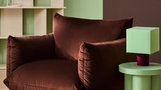 Close-up image of a chocolate brown modern accent chair next to a mint green side table with a mint green and burgundy lamp.