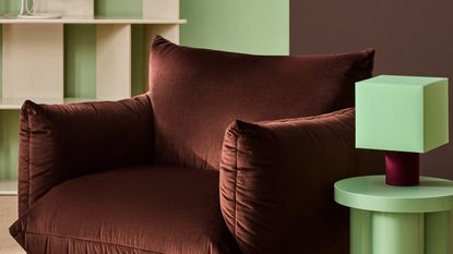 Close-up image of a chocolate brown modern accent chair next to a mint green side table with a mint green and burgundy lamp.