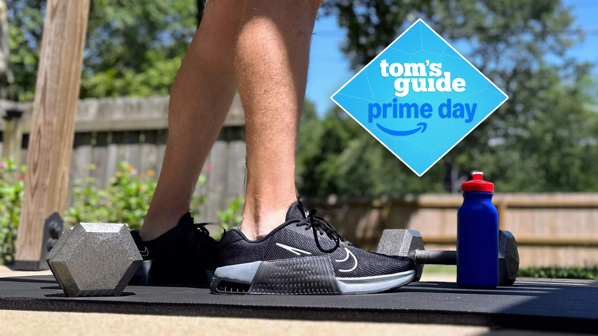 Person wearing Nike Metcon 9 standing on mat outdoors with dumbbell by feet, Prime Day badge