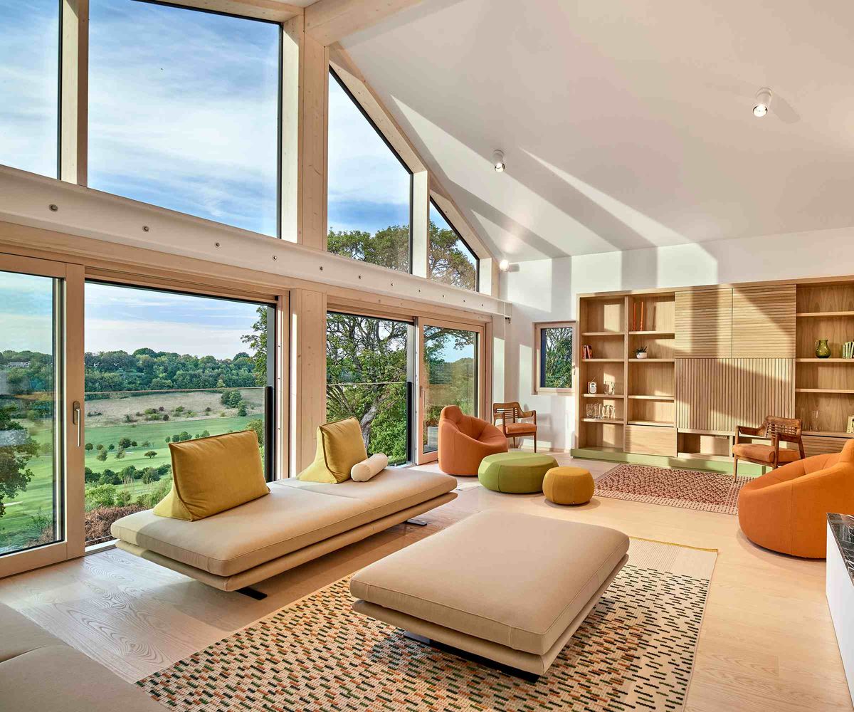 A large living room with vaulted ceiling and glazed gable end overlooked countryside. The room features low Japanese-style sofas and a large bookcase.