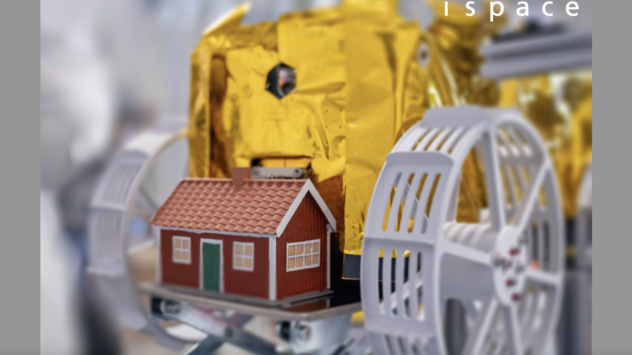 closeup photo of a golden mini moon rover, which has a small red and white house on its bumper