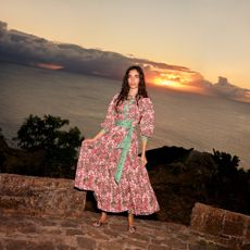 Model wearing a colourful long dress and sandals infront of a sunset