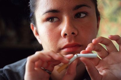 A young woman breaking a cigarette in half