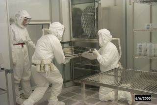 Genesis solar wind sample curators at NASA's Johnson Space Center handle collectors in the ultraclean Genesis cleanroom. Curators wore suits to keep the collectors clean. The wearer's body is totally enclosed, and exhaled air is filtered through a HEPA filter, seen on the rear side belt. Genesis samples are the first extraterrestrial materials returned to Earth by NASA since the Apollo program, which ended in the early 1970s.