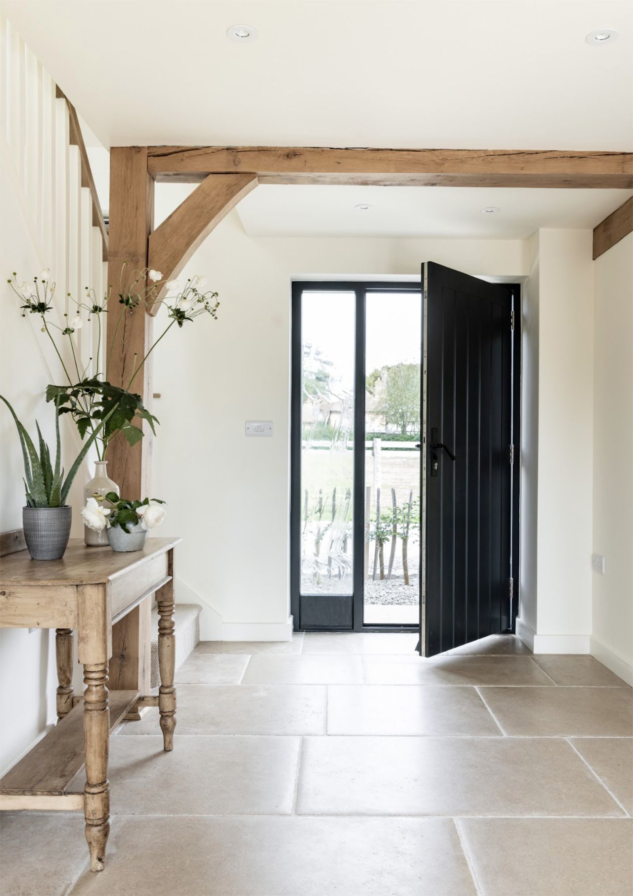 The entrance hall of a small oak framed home with a console table, exposed beams and an open front door