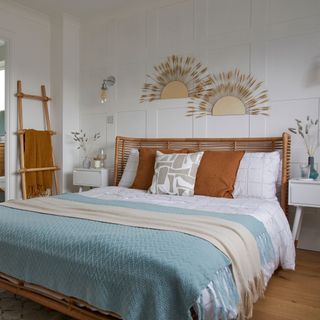 white bedroom with wall panelling wall lights rattan bed frame blue throw