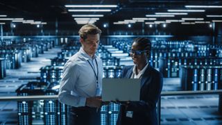 man and woman on laptop in front of large data center