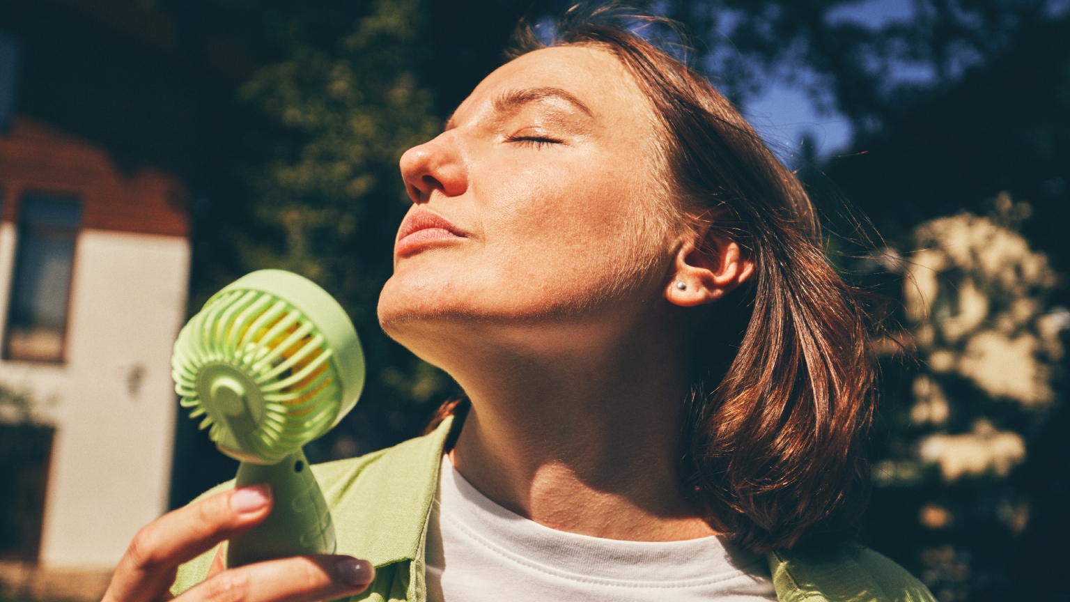 a woman with short red hair holding a cooling fan up to her face